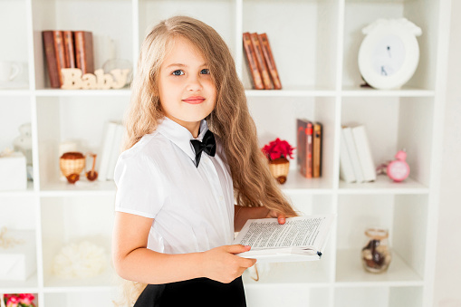 little schoolgirl in school uniform holding the textbook