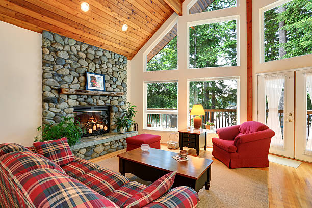 living room interior in luxury home with tall vaulted ceilings, beautiful dark hardwood floors, trim, and trusses, and view of kitchen. Lush green trees make up exterior view.