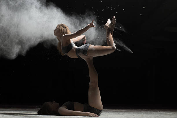 istock Two woman acrobatics posing and sprinkle flour on black background 590075686