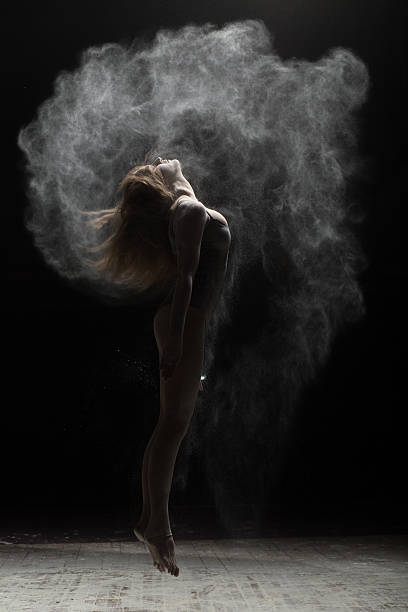 istock Flexible woman jumping and sprinkle flour on black background 590076270