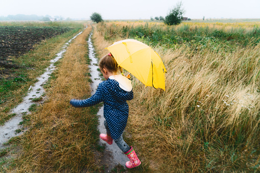 Little Caucasian girl walking with umbrella under the rain 