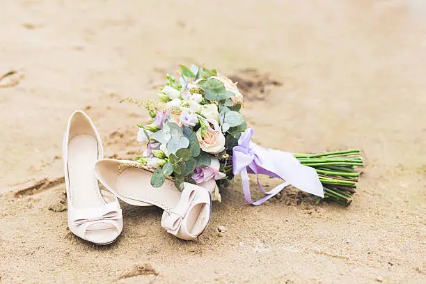 Beautiful boho rustic composition with a bridal bouquet and wedding shoes standing on a beach sand