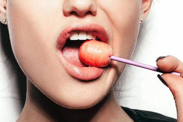 Woman licking a red shiny lollipop. Close up against white background, not isolated