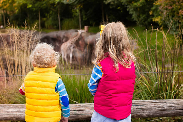 Cute boy and girl siblings smiling at camera  against rustic wood background outdoors on cold day with copy space.