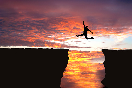 Silhouette of man jumping from one cliff to another cliff with excitement