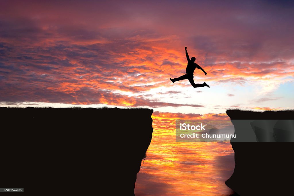 Jumping into cliff gap Silhouette of man jumping from one cliff to another cliff with excitement Jumping Stock Photo