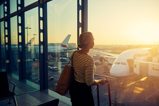 Shot of a young woman looking through the window of an airport departure lounge