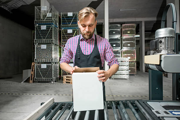 Packer on the packaging line Handsome packer in working apron with box on the packaging line at the manufacture. wine shipping stock pictures, royalty-free photos & images