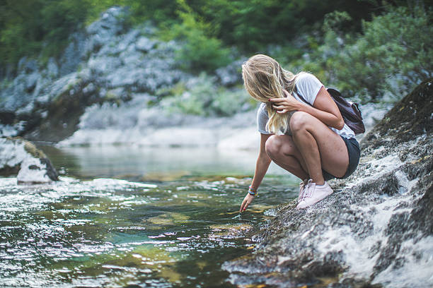 Young girl relaxing next to a mountain lake and touching the water