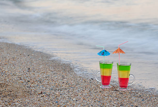 due cocktail con cannucce nella sabbia sulla riva del mare - umbrella two objects cocktail drink foto e immagini stock