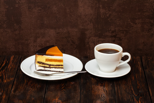 Orange cake slice and coffee cup on dark wooden background