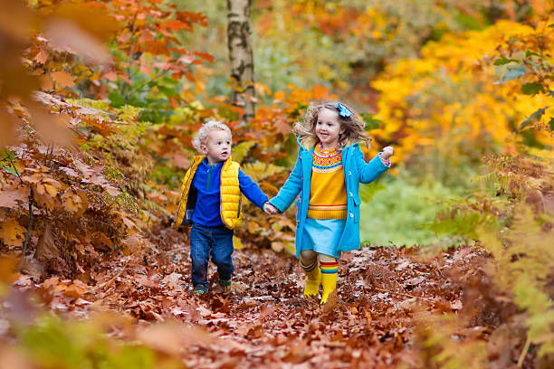 Happy children playing in beautiful autumn park on cold sunny fall day. Kids in warm jackets play with golden  leaves.