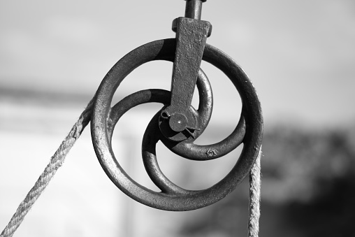 Close up view of an old metal pulley used to bring water to the surface of a well with a bucket. Black and white.