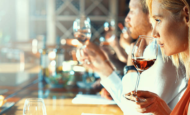 Wine tasting. Closeup side view of group of people tasting wine samples at a winery. They are seated side by side in well lit tasting room. They are smelling wines and analyzing visual appearance before actual tasting. winetasting rose wine wineglass elegance stock pictures, royalty-free photos & images