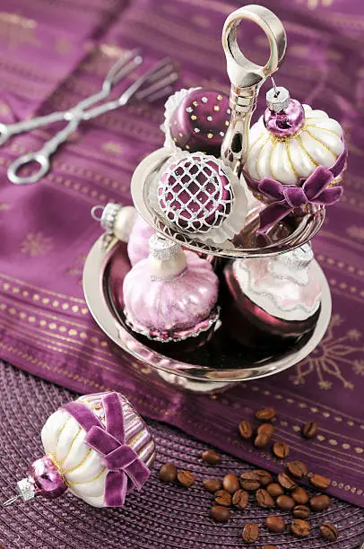 serving christmas ball muffins in a etagere with cake tongs. purple tablecloth.  coofee beans on ground.