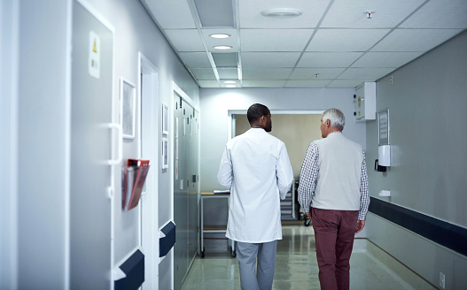 Rearview shot of a doctor talking to a senior patient while walking through the hospital corridor