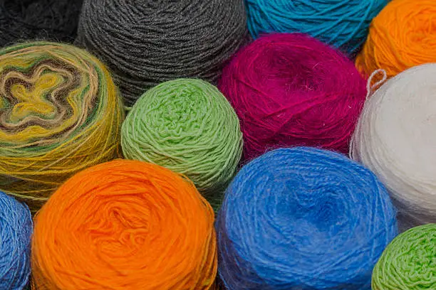 Many small balls of wool of rainbowcolors on the wooden table.