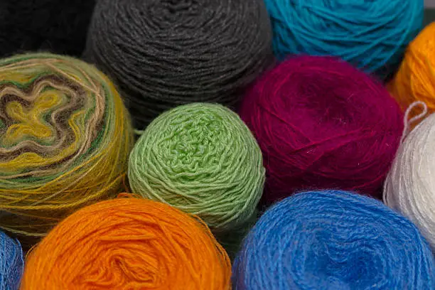 Many small balls of wool of rainbowcolors on the wooden table.