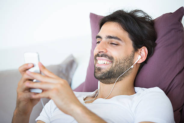 istock Smiling man relaxing in a bed and using MP3 player. 590252718