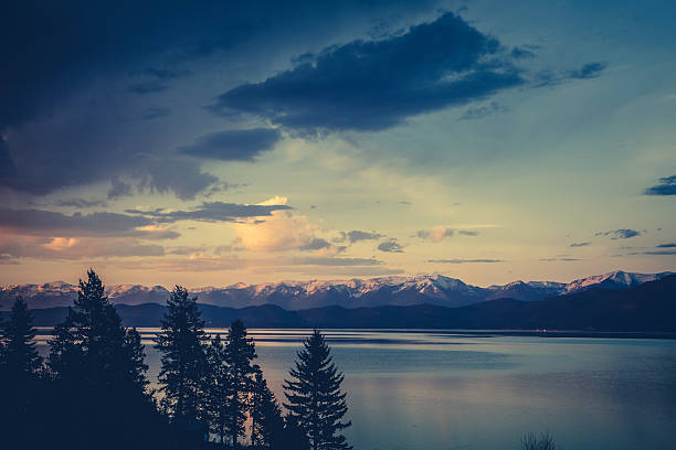 A beautiful nature scene looking out across Flathead Lake, Montana at dusk, just after sunset. The Swan and the Mission mountain ranges can bee seen across the lake. Warm and cool colors of the clouds in the sky are reflected on the water surface below. No people in this high resolution color photograph with copy space and horizontal composition.