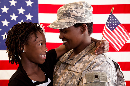 USA Military mom gets a big hug from her daughter.  Excited homecoming for this family.  American flag background.  National holidays:  Veteran's Day, Memorial Day.