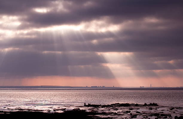 View of Grimsby from Spurn Point, East Yorkshire View of Grimsby across the River Humber from Spurn Point, East Yorkshire, showing sunburst and clouds humberside stock pictures, royalty-free photos & images