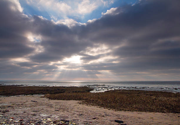 Sunburst and clouds on the shore of the River Humber at Spurn Point nature reserve, East Yorkshire, UK