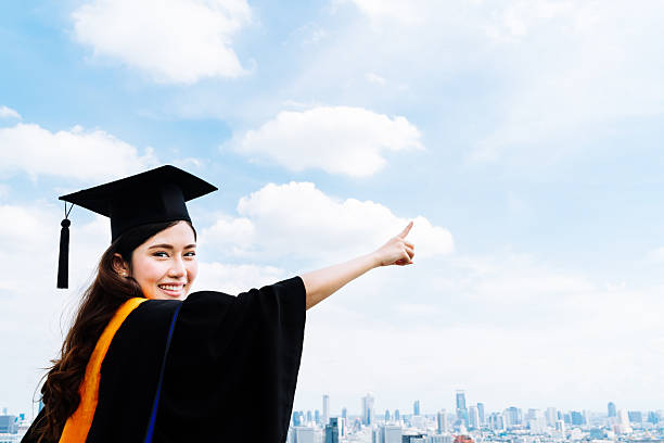 Asian university graduate student woman pointing copy space on sky stock photo