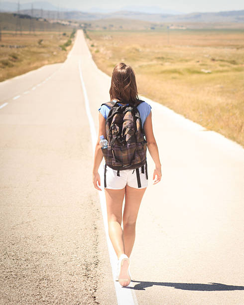 istock Woman backpacker walking on road 590292280