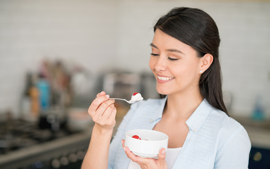 Young woman at home eating a healthy breakfast with strawberries and yogurt