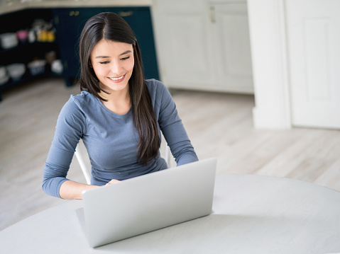 Latin woman working online from home using a laptop computer and looking happy