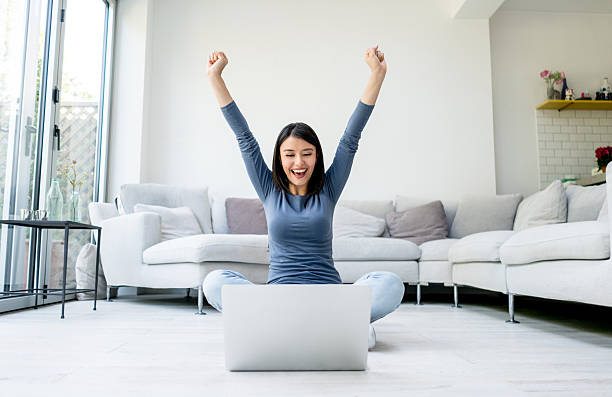 Excited woman working on a laptop from home Excited woman with arms up working on a laptop computer from home - online success concepts excitement laptop stock pictures, royalty-free photos & images