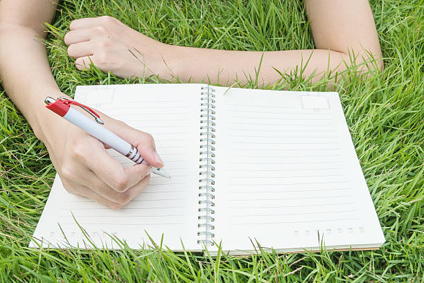 istock Closeup woman lying on grass writing on note book 590580238