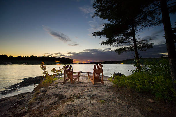 Two Muskoka chairs sitting on a rock at sunset stock photo