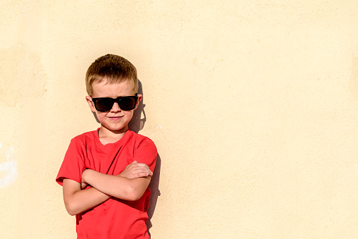 Portrait of young boy wearing sunglasses  and leaning against wall like a boss