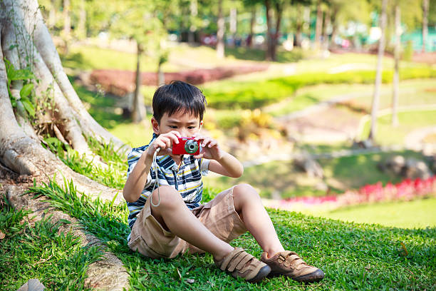 Cute smiling baby boy on the green meadow. Close up portrait of fun happy boy. Kid in the sitting on the green grass and looks at camera.