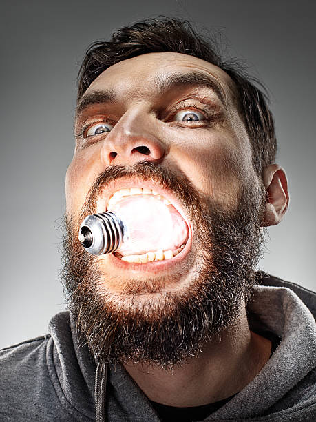 The funny caucasian man with glowing bulb in his mouth on gray background