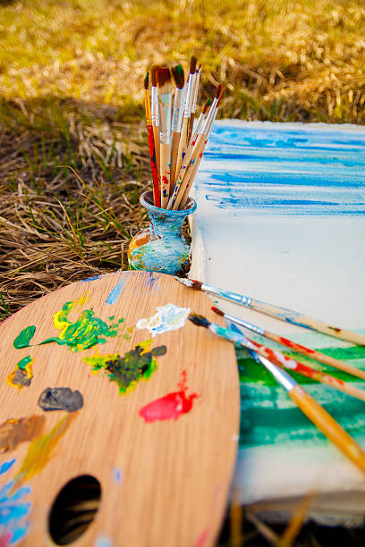 istock Palette with paints and brushes on picture on grass background 590600036