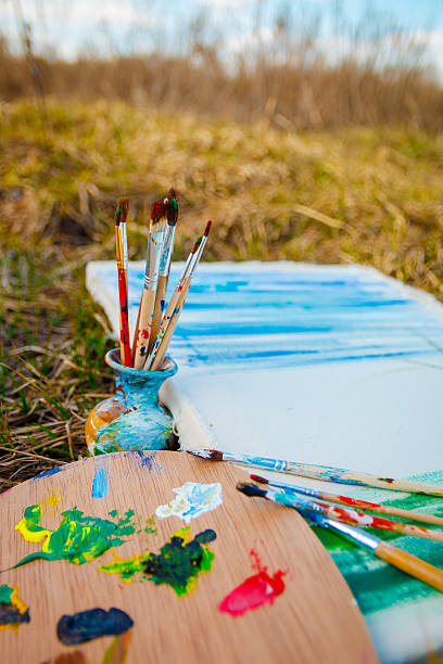 istock Palette with paints and brushes on picture on grass background 590600134