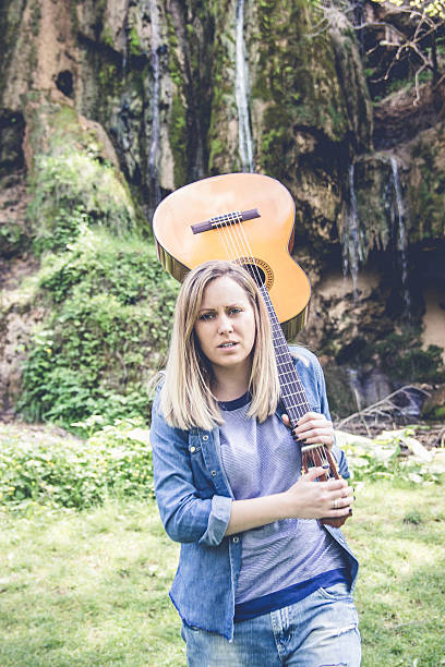 istock Young woman playing guitar by waterfall in summer 590600140