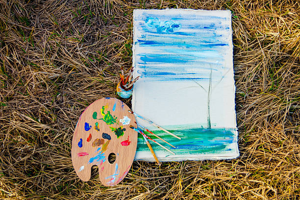 istock Palette with paints and brushes on picture on grass background 590600302