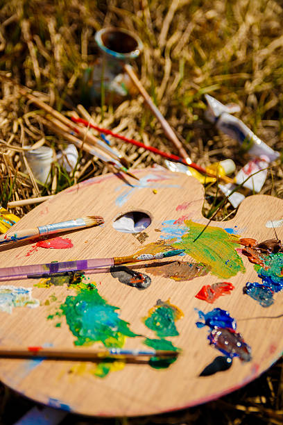 istock Palette with paints and brushes on picture on grass background 590600428