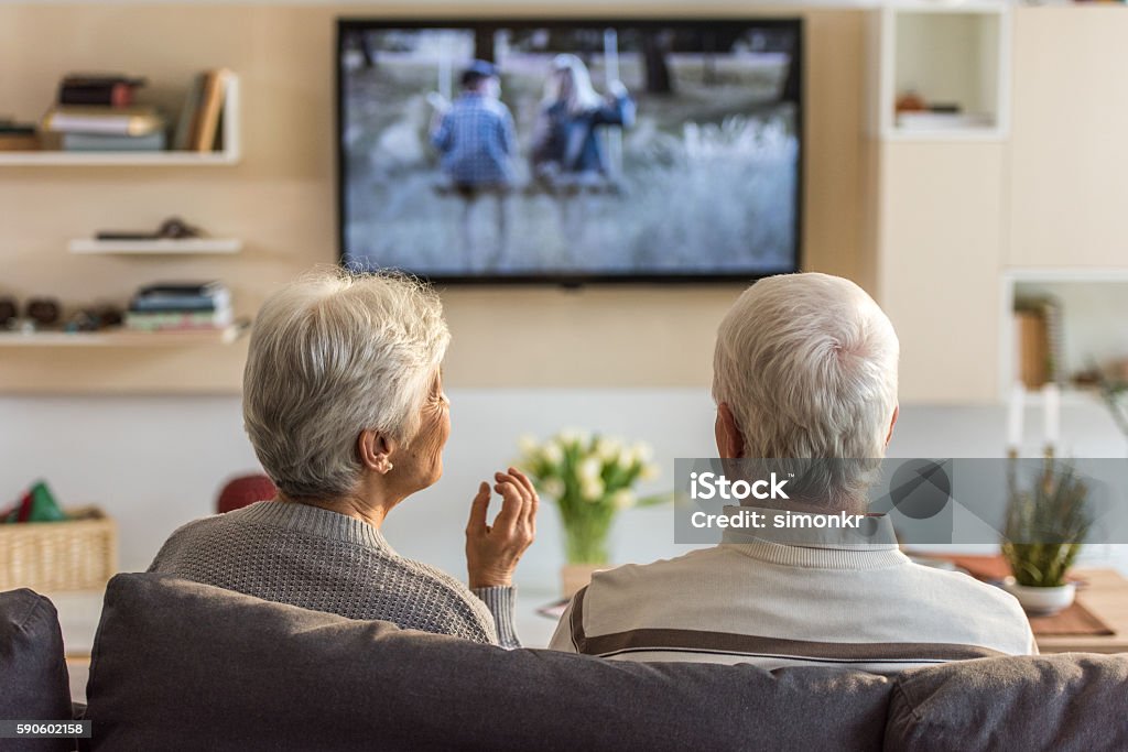 Senior couple watching television show Senior couple sitting on sofa and watching television show at home. Watching TV Stock Photo