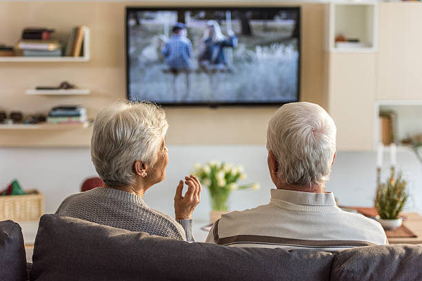 Senior couple watching television show Senior couple sitting on sofa and watching television show at home. watching tv stock pictures, royalty-free photos & images