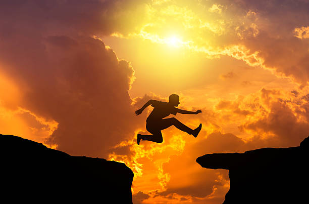 istock silhouette man jumping through the gap on sunset 590606278