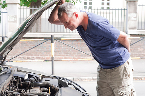 A man looking under the hood. A business man having a bad day checks under the hood of his car to figure out what the problem is.