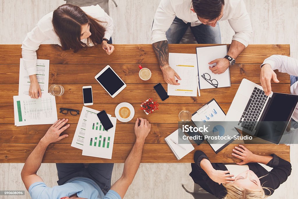 Group of busy business people working in office, top view Group of busy business people working in office, top view of wooden table with mobile phones, laptop, tablet and documents papers with diagram. Men and women team together have brainstorm discussion. Motion Stock Photo
