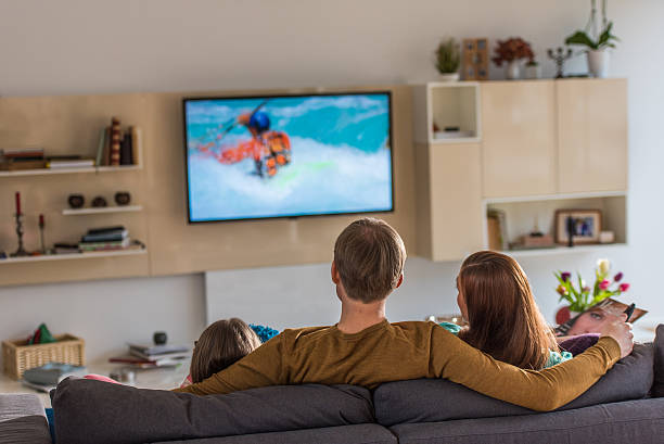 Family sitting on sofa Family sitting on sofa and watching television show. couch back stock pictures, royalty-free photos & images