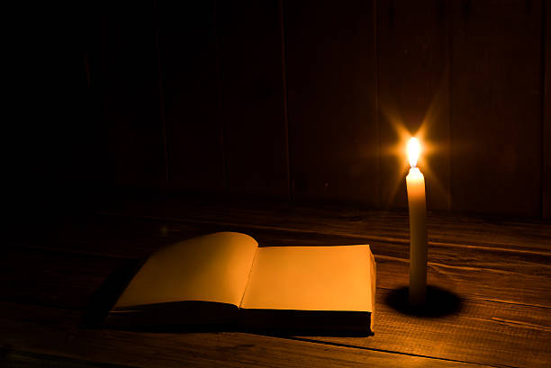 istock Old antique book opened with burning candle near. 590615592