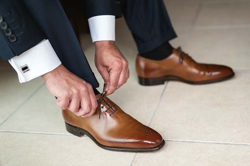 Horizontal color low section view image of groom tying up brown leather shoes.